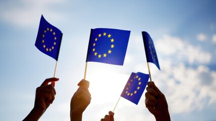 Hands holding European Union flags in the air against bright sky representing unity, civic engagement, and support for EU values and identity