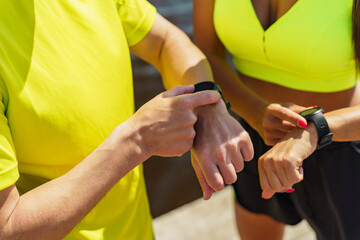 Wellness enthusiasts checking fitness trackers during outdoor workout session on sunny day