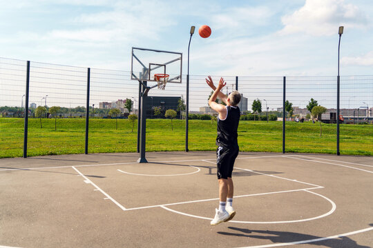 Basketball player shooting a three-pointer on an outdoor court in summer sunshine