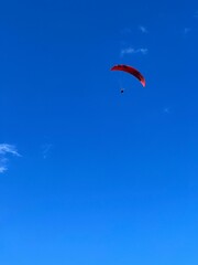 Man Flying with a red parachute, paraplane in the air. Bright, clear sky, in the background. Picturesque beach. Space, nature concept, retreat, sport, hobby, recreation