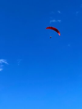 Man Flying with a red parachute, paraplane in the air. Bright, clear sky, in the background. Picturesque beach. Space, nature concept, retreat, sport, hobby, recreation