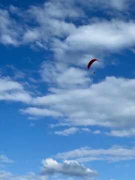 Man with a red parachute, paraplane in the air. Bright, clear sky, with white fluffy clouds in the background. Picturesque beach. Space, nature concept, retreat, sport, hobby, recreation