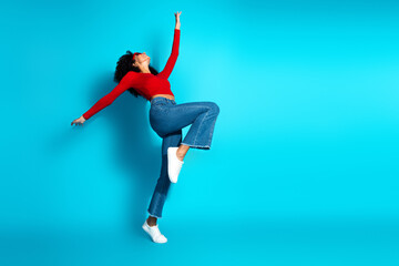 Woman in red top and jeans making expressive dance movement against vibrant blue background