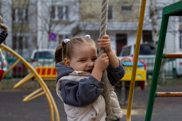 A girl child climbs a rope on a playground, enjoying outdoor activities, developing strength and coordination. Smiling and playing, the child personifies the joy of an active childhood.
