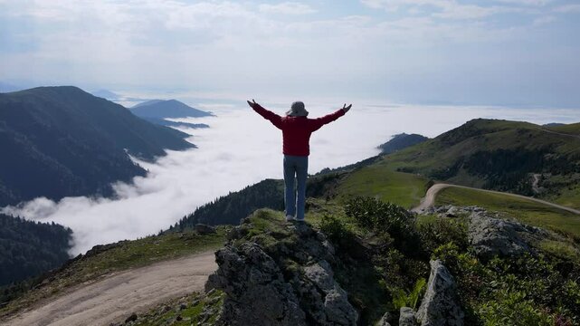 Footage of woman standing on a mountaintop, arms outstretched, gazing at nature.