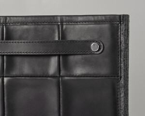 Black leather bag detail showing stitching and metal button