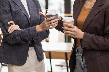 Two Asian businesswomen standing holding cups hot coffee to drink while discussing business investment together in conference room during a break. businesswomen standing holding paper cups hot coffee