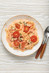 Seafood linguine pasta in creamy sauce with shrimp and cherry tomatoes, garnished with fresh parsley, served on white wooden background with cutlery top view