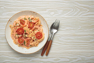Seafood linguine pasta in creamy sauce with shrimp and cherry tomatoes, garnished with fresh parsley, served on white wooden background with cutlery top view, copy space