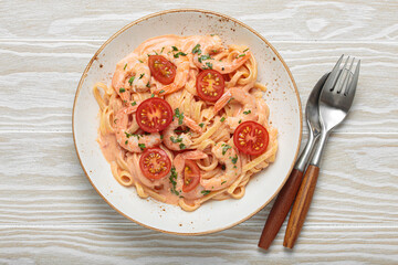 Seafood linguine pasta in creamy sauce with shrimp and cherry tomatoes, garnished with fresh parsley, served on white wooden background with cutlery top view