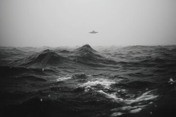 Eerie monochrome seascape with choppy waves and an unidentified flying object hovering above, shrouded in a mysterious, misty atmosphere during daytime.