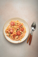 Seafood linguine pasta in creamy sauce with shrimp and cherry tomatoes, garnished with fresh parsley, served on a light warm beige background with cutlery top view