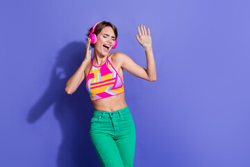 Fototapeta premium Photo of young energetic girl in pink crop top stylish outfit dancer likes wireless headphones isolated on violet color background