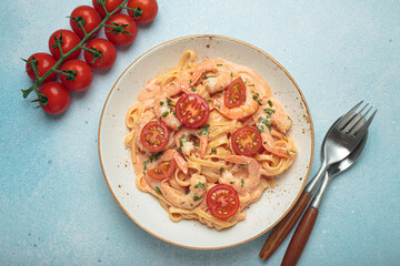Seafood linguine pasta in creamy sauce with shrimp and cherry tomatoes, garnished with fresh parsley, served on a light blue background with cutlery top view