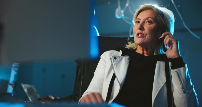 Night, hacker and phone call at computer for cyber crime, negotiation or contact for scam. Mature woman, team and underground with technology for data phishing, blackmail threat or ransomware in dark