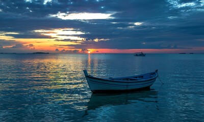 Seascape in the sunset with a small boat against dark blue sky and cloudy sky