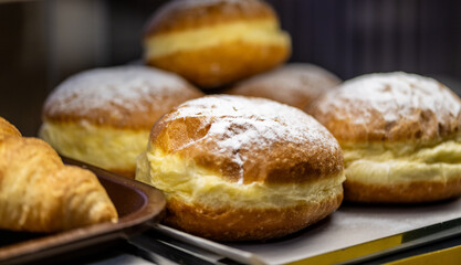 Traditional European cream-filled pastries dusted with powdered sugar displayed alongside golden croissants on bakery shelf, macro food photography