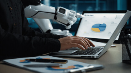 Fototapeta na wymiar A human hand types on a laptop in a modern office setting, with a robot arm assisting and charts displayed on the screen, symbolizing technology collaboration.Noogenesis