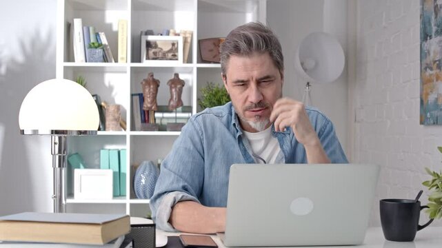 Older white man sitting at desk using laptop in home office. 50s businessman on video chat conference call and working from home.