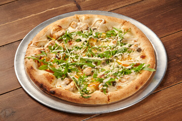 Delicious pizza with chicken, arugula, and parmesan cheese on wooden table