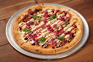 Delicious gourmet pizza with raspberries, almonds, balsamic glaze and basil on wooden table