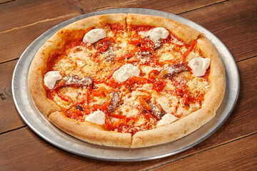 Delicious pizza with anchovies, red peppers, and creamy sauce resting on wooden table