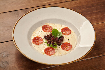 Creamy polenta with sliced pepperoni, parmesan, and fresh herbs on rustic wooden table