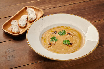 Creamy mushroom soup decorated with mushrooms and parsley with toasted bread on wooden table