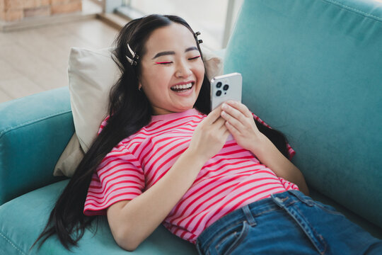 Young woman relaxing on a couch at home enjoying lighthearted moments with her smartphone, experiencing leisure and happiness indoors
