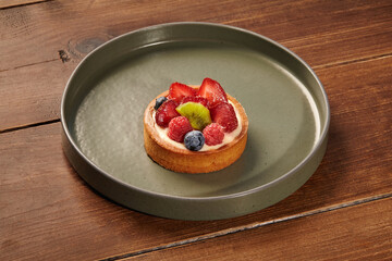 Delicious fruit tartlet on a green plate on wooden table