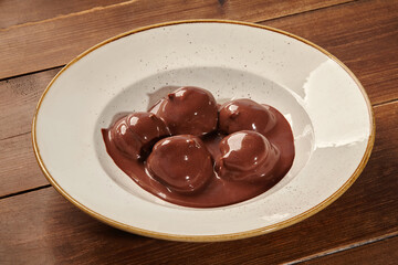 Chocolate profiteroles bathing in a rich chocolate sauce on rustic wooden table