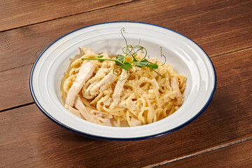 Creamy pasta dish with tender chicken, rich cheese sauce, parmesan, and pea sprouts, served on a rustic wooden table