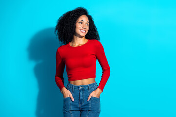 Young woman in red top smiling confidently against a vibrant blue background, showcasing trendy...