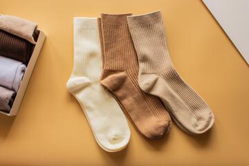 Three pairs of ribbed socks in cream, brown, and beige colors are arranged on warm yellow background, highlighting their cozy texture and stylish design.