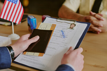 Approving visa application with passport and approved document, focus on hands handling important paperwork, American flag in background