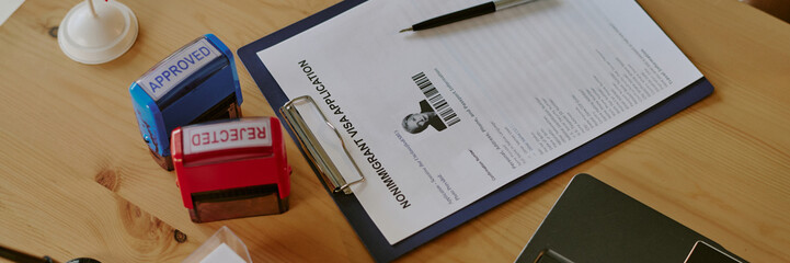 Plakat Nonimmigrant visa application form with photo and biometric data, surrounded by approved and rejected stamps, and pen on wooden surface highlighting immigration process