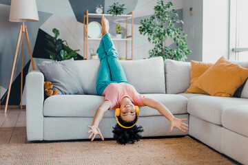 Young woman enjoying leisure time indoors, wearing headphones and upside down on a sofa in a bright...
