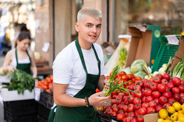 Portrait of young man seller with green onions in her hands - work in a grocery supermarket