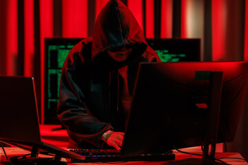 A hacker operates in a dark room, stealing sensitive data through cybercrime — representing one...