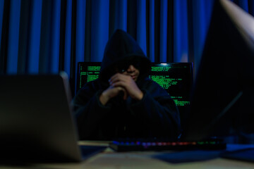 A hacker operates in a dark room, stealing sensitive data through cybercrime — representing one...