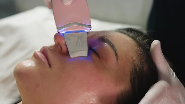 Beauty specialist wearing gloves glides ultrasonic wand over client face to gently extract pimples and impurities during advanced skin treatment session in luxury modern spa environment