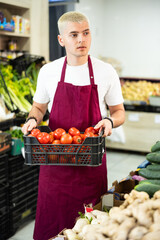 Male salesperson in an apron carefully places ripe tomatoes on a supermarket counter