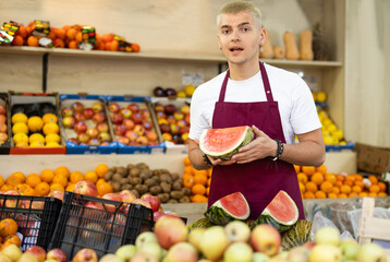 A male salesman in an apron carefully places ripe watermelons on a supermarket counter