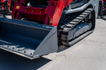 Industrial compact skid steer loader with rubber tracks on hard asphalt in bright day ready for...