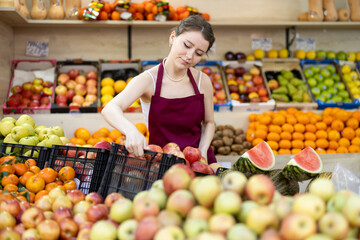 Female seller has received a supply of fresh apples and puts them on the counter, checking the quality. Fresh seasonal fruit in the supermarket