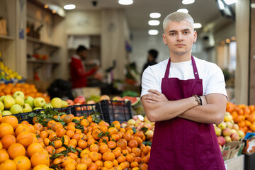 Young guy seller in apron posing at vegetable market
