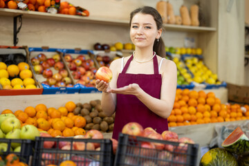 Woman saleswoman stands in the grocery department and offers ripe seasonal apples. Supermarket worker offering fruits