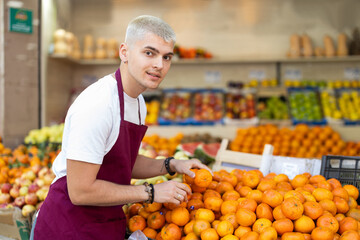 Working in supermarket - male salesman sorts through ripe tangerines on the display case