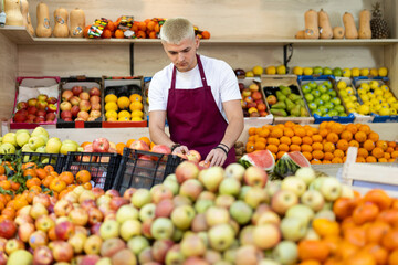 Supermarket employee carries a box of ripe apples