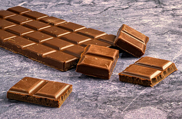 Pieces of milk chocolate on stone background